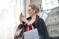 Enjoying life on a budget. Stylish woman with shopping bags using smartphone in Milano, Italy. Perfect urban tech and fashion capture.