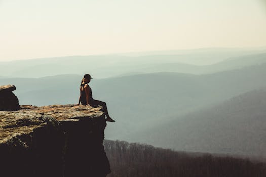Woman sitting on a cliff edge overlooking a vast mountain landscape in Arkansas.