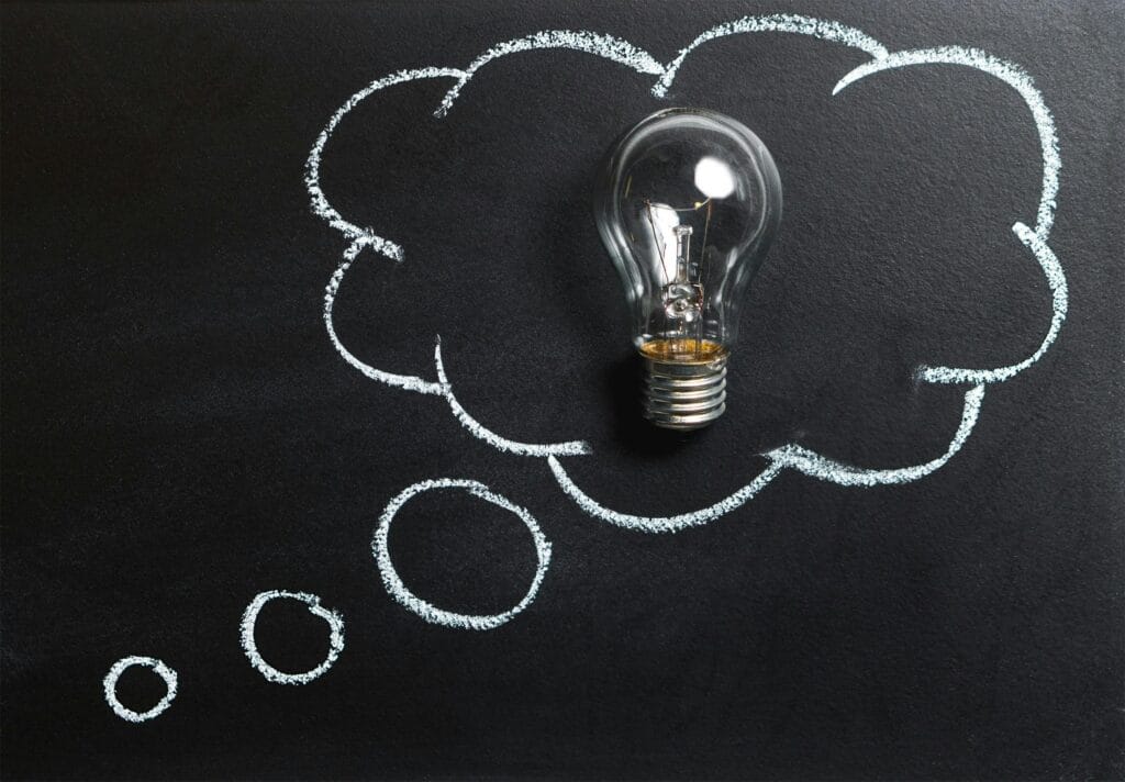 5 financial terms everyone should know. Light bulb laying on chalkboard with drawn thought bubble, symbolizing creative ideas.