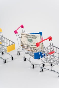 Miniature shopping carts filled with US dollar banknotes on a white background, representing commerce and financial concepts.
