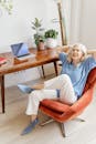 Senior woman in modern office setting, relaxing in a chair with a laptop on a desk.